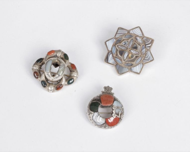 Suite de 3 broches en argent : la 1re en forme d’étoile sertie d’agate rubanée ; la 2e formée d’enroulements sertis de jaspes et d’agates ; la 3e gravée de feuillages et d’une boucle de ceinture, sertie de jaspes et d’agates. Travail écossais du XIXe siècle. Poids brut : 35,7 g (manque)