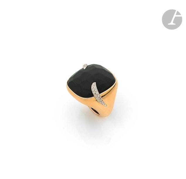 POMELLATO
Importante bague»Victoria»en or 18K (750), ornée d’un cabochon de jais facetté serti clos entre deux griffes d’or gris serties de diamants ronds de taille brillant. Signée. Dans sa pochette en soie chartreuse.Tour de doigt : 51. Poids brut : 42,7 g