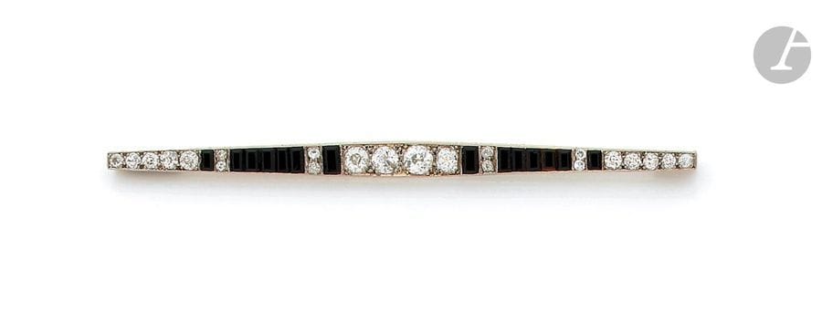 Broche-barrette en or gris 18K (750), sertie de diamants ronds de taille ancienne scandés d’onyx calibrés. Travail des années 1920. Longueur : 10 cm environ. Poids brut : 9,1 g (chocs)