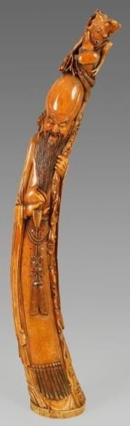 Importante statuette de Shou Lao en ivoire à patine jaune et incrustation de cabochons, debout tenant dans sa main droite une pêche de longévité et s'appuyant sur sa canne, chargée de doubles gourdes. Au revers de la base la marque apocryphe «Da Ming». Chine, XXe siècle. Hauteur: 88 cm.