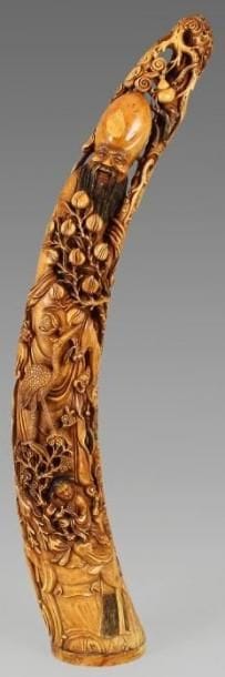 Importante statuette de Shou Lao en ivoire à patine jaune, debout sur un rocher s'appuyant sur sa canne, tenant une branche chargée de pêches de longévité, accompagné d'un enfant chevauchant un cerf et d'une grue. Au revers de la base la marque apocryphe «Da ming». Chine, XXe siècle. Hauteur: 87 cm.