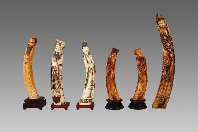 Importante statuette de jeune femme en ivoire à patine jaune et incrustations de cabochons de verre, tenant dans sa main gauche un éventail rigide et dans la droite une branche de pivoine. Au revers la marque apocryphe «Da ming». Chine, XXe siècle. (Eclats à la coiffe). Hauteur: 90 cm.