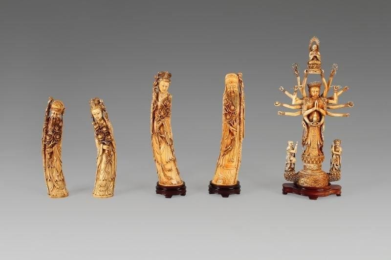 Couple d'immortels debout en ivoire à patine jaune et incrustation de cabochons de verre, tenant des branches de pivoines, l'homme s'appuyant sur sa canne. Chine, XXe siècle. Hauteur: 45 cm. Socles en bois.