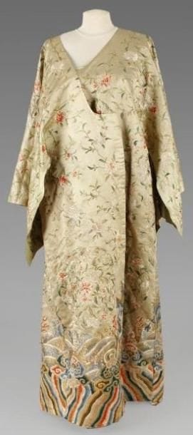 Robe en soie à fond beige brodée de pivoines en blanc et rouge dans leur feuillage au-dessus des vagues. Représentation de lingzhi en bas du vêtement ainsi que d'une frise géométrique polychrome. Canton, XIXe siècle. (Accidents). Hauteur: 137,5 cm.
