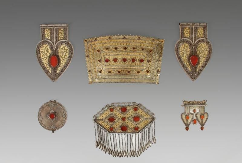 Pendentif dorsal, Gosa-Asyk, Ersari, à double coeur, en argent, à décor incisé, filigrané, appliqué, ajouré, et partiellement doré. Décor délimité par des frises à une tresse filigranées; l'ensemble est rehaussé de six cabochons en cornaline, en forme de goutte ou en ovale, sur un fond de demi-palmettes. La partie supérieure est surmontée d'une frise de cornes de bouquetins. Turkestan, XXe siècle. Hauteur: 11,8 cm. - Longueur: 11,2 cm.
