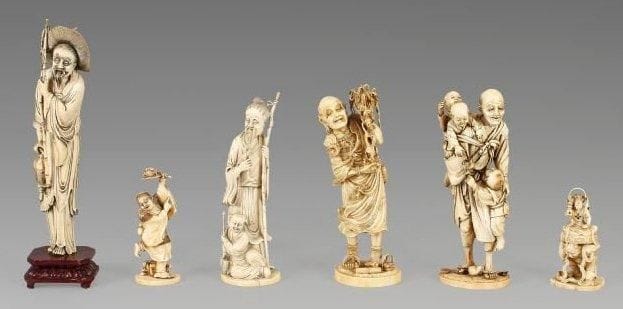Okimono en ivoire à patine jaune, personnage debout portant deux enfants sur son dos, un autre par sa ceinture. une poupée Daruma et une paire geta à ses pieds. Signé Toshigawa. Japon, XIXe siècle. (Restauration au pied et petits accidents). Hauteur: 26 cm.