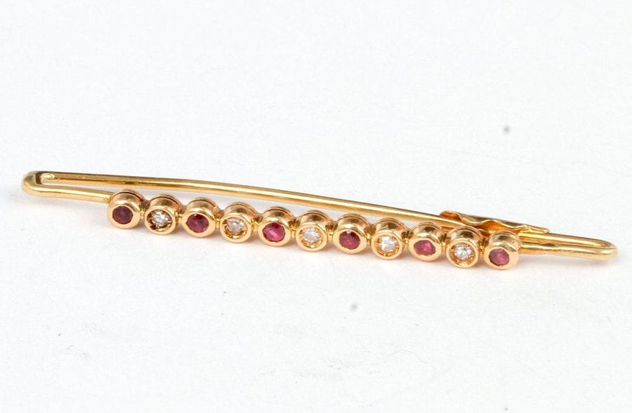 Broche-barrette en or 18K (750), sertie d’une ligne de ru et de diamants alternés. Longueur : 4,5 cm environ. Poids brut : 2,5 g