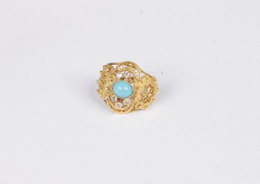 18K (750) gold ring woven with filigree motifs, set with a cabochon turquoise, decorated with colourless glass paste. Finger size: 51. Gross weight: 5.4 g (missing, shocks)