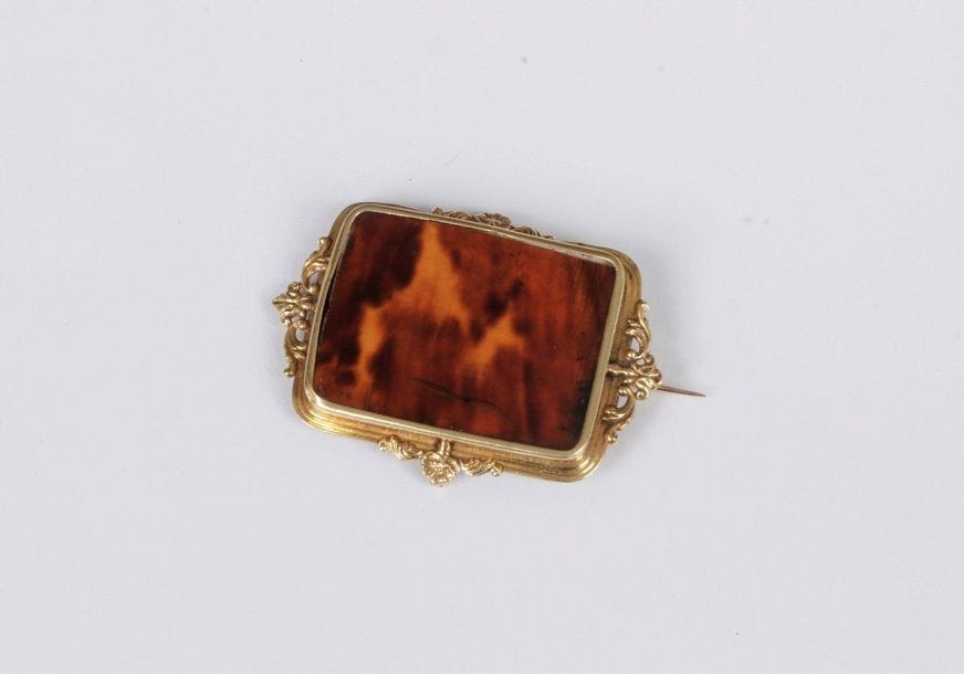 Broche en or 18K (750) ornée d’une lame d’écaille de tortue, la monture ciselée de motifs rocaille. Travail français du XIXe siècle. Dimensions : 5,3 x 3,5 cm environ. Poids brut : 7,8 g (déformations)
