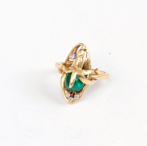 Bague en or 18K (750), ornée d’une fleur, le cœur en émeraude, le pistil piqué de diamants de taille ancienne. Travail du début du XXe siècle. Tour de doigt : 58. Poids brut : 7,8 g (manques de matière)