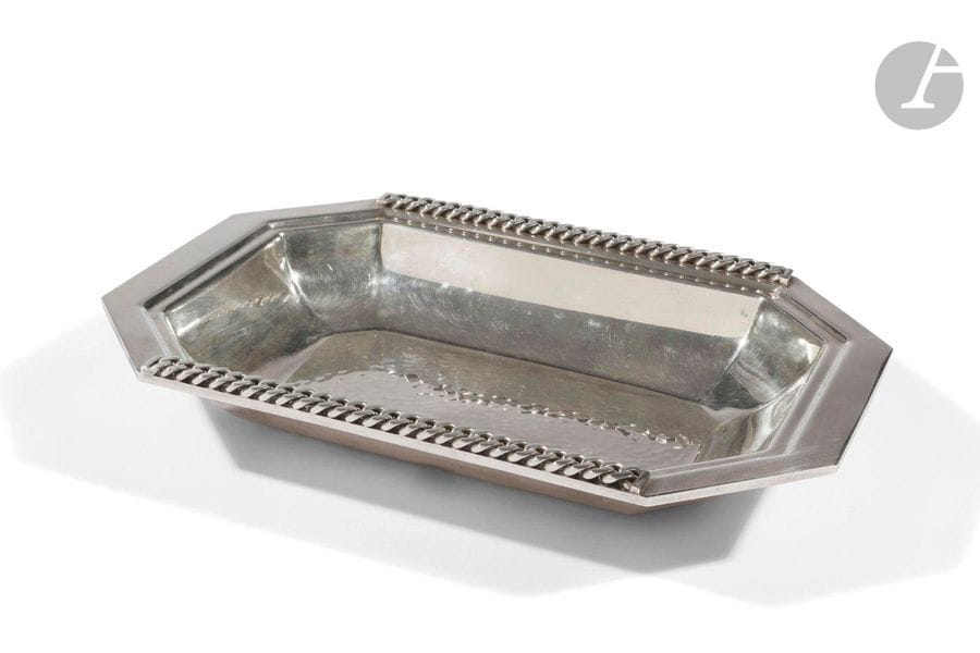 JEAN DESPRÉS (1889-1980
)Bread basket in silvery metal. The hammered bottom, the holds with flat-linked curb chain motifs in applications. Signed J. DESPRÉS, with the point on the reverse. H. 4,5 cm - L. 30 cm - W. 21 cm
