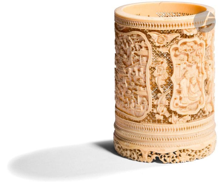 CHINE, Canton - XIXe siècle
Pot à pinceaux en ivoire sculpté et réticulé à décor de panneaux polylobés ornés de pavillon, pagode et scène de vie sur fond de tiges fleuries. (Gerces naturelles). 
H. 14 cm ; diam. 9,7 cm
