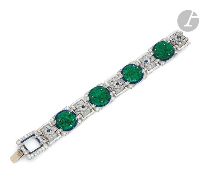 Bracelet en platine et en or gris 18K (750), articulé de maillons quadrangulaires dont 4 sertis d’un jade repercé et sculpté de fleurs dans des feuillages, entouré d’un filet d’émail bleu, agrémenté de diamants ronds de taille ancienne, entre des maillons sertis de diamants dessinant des fleurs, les coeurs piqués d’un saphir cabochon. Travail français des années 1930. Traces de numéro.
Dimensions : 2 x 17,8 cm environ.
Poids brut : 62,8 g