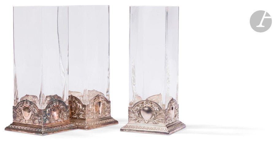 PORTUGAL - PORTO XXe siècle
Suite de trois vases en cristal monture en argent 925 ‰. Le cristal de forme carrée repose sur une monture repoussée d’une frise godronnée, prolongée par un décor estampé ajouré figurant des blasons dont le champ est laissé libre, alterné de branches de lauriers sur les quatre faces.
Orfèvre : TOPAZIO
Poids brut : 7608,50 g - hauteur : 32 cm
état : un vase accidenté (cristal)