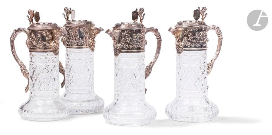 PORTUGAL - PORTO XXe siècle
Ensemble de quatre aiguières en cristal taillé et monture en argent 925 ‰. De forme circulaire, le cristal reçoit dans sa partie supérieure une frise repoussée sur deux faces de scènes figurant des putti dansant et jouant encadrant un bec verseur souligné d’une tête de Bacchus, et une anse à l’imitation d’un cep de vigne. L’appui-pouce du couvercle à charnière figure un lion héraldique tenant un blason dont le champ est laissé vierge de gravure.
Orfèvre : TOPAZIO
Poids brut : 6883,6 g - hauteur : 28,5 cm - diamètre de la base : 13,5 cm
