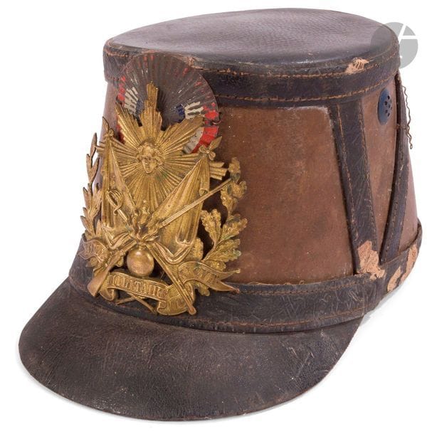 Shako de l’ESM Saint-Cyr modèle 1872. 
Fût à garnitures en cuir. Cocarde tricolore. Étiquette « Louis Aubert (…) ».
Plaque dorée. 
Dans l’état.