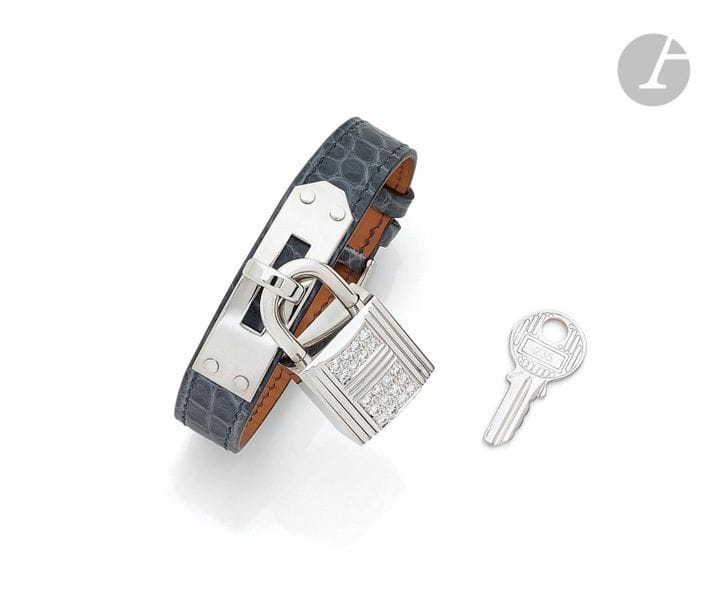 HERMÈSCadenas
in 18K (750) white gold paved with 40 round brilliant-cut diamonds; it is fitted with its 18K white gold key and held by a Kelly bracelet in white crocodile and steel. Signed. French work of the early 21st
century.

Dimensions:

about

3.3 x 1.9 cm

.


Gross weight: 59.4 g








