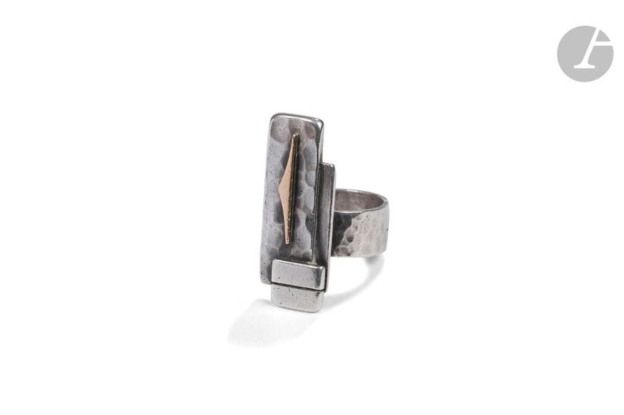 JEAN DESPRÉS (1889-1980)
Motif géométrique
Bague moderniste en argent et or. L’anneau martelé, l’entretoise cylindrique, la plateforme rectangulaire composée d’un motif géométrique sur fond martelé et recevant des barrettes traitées lisses. Signée J. DESPRÉS à la pointe à l’intérieur de l’anneau et porte les poinçons de Maître Orfèvre et de garantie à l’extérieur. Poids:16 g