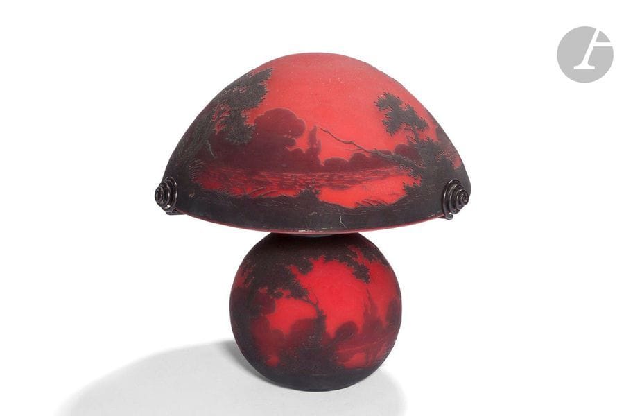 MULLER FRÈRES À LUNÉVILLE 
Paysage lacustre arboré
Lampe champignon; la base de forme boule, l’abat-jour en obus. Épreuve en verre multicouche, le décor tournant dégagé à l’acide traité noir sur fond rouge. Support d’abat-jour à trois branches terminées par des enroulements en métal patiné noir. La base et l’abat-jour chacun signé MULLER FRES Lunéville, en réserve gravé en camée à l’acide. H.27cm 
