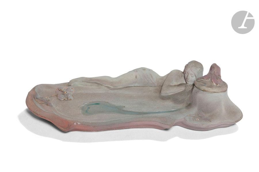 CÉRAMIQUE DE CHARENTON – MODÈLE DE CH.HAAG (XIXe-XXe)
Rêverie au bord de l’eau 
Encrier. Épreuve en céramique émaillée mat et brillant et réhaussée à l’or. Complet de son réceptacle à encre en verre. Signé Ch.HAAG sur le pourtour, porte le cachet de la manufacture en creux sous la base. H.6,5cm – L.25cm – 12,5cm 