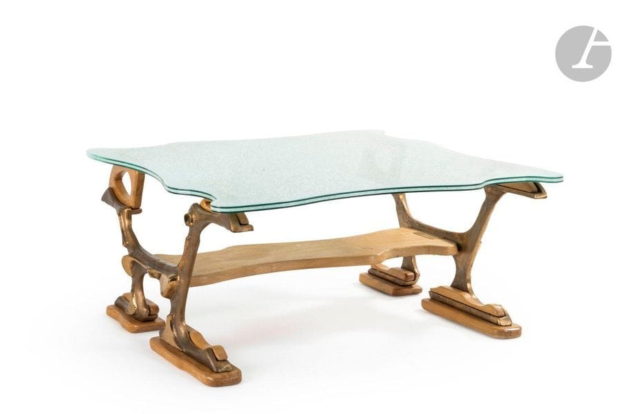 GINO (NÉ EN 1937) SCULPTEUR & MICHEL RIOU DESIGNER & PASCAL THOUVENEL ÉBÉNISTE
Sans titre
Importante table de salon à deux plateaux. Les jambages réalisés à partir de sculptures en bronze de Gino; les patins longitudinaux, la tablette d’entrejambe et les réceptions du plateau en chêne sculpté. Le dessus au pourtour en découpe réalisé en verre sandwich; la feuille centrale en verre Securit brisé à l’aspect crispé. Signée GINO sur une partie en bronze, porte la plaque métallique avec les mentions suivantes: Table dessinée par Michel RIOU dit Mimi et réalisée par Pascal THOUVENEL dit T.T.B.A. H.55cm - L.120cm - L.120cm
