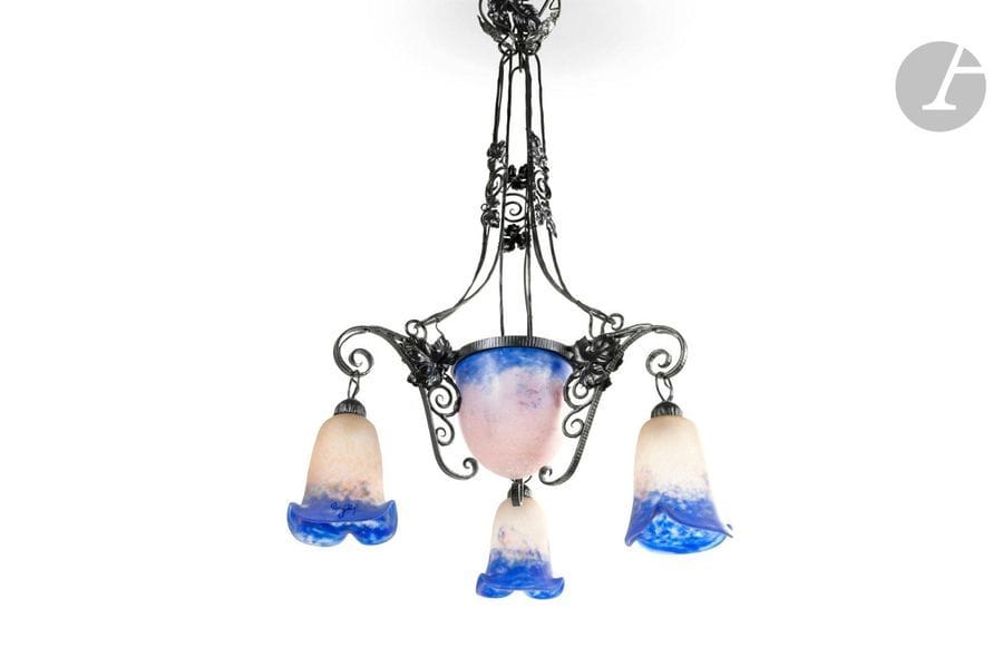 DEGUÉ (VERRERIE D’ART FONDÉE PAR DAVID GUÉRON) & TRAVAIL FRANÇAIS 1925/30
Suspension à quatre lumières; un obus central et trois tulipes. Monture en fer forgé aux motifs de vigne. L’obus et les tulipes en verre marmoréen bleu sur fond gris-blanc nuancé de rose. Chaque verrerie marquée DEGUE. H.93cm – L.42cm – L.42cm