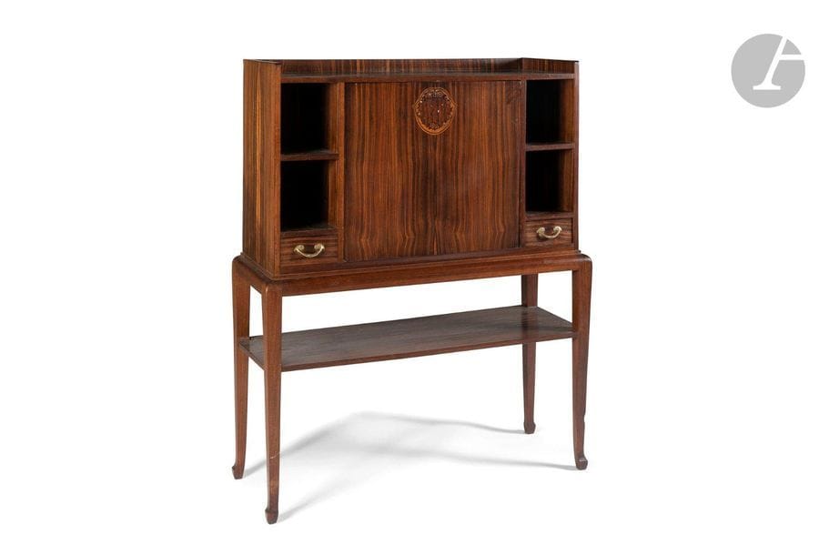 LOUIS MAJORELLE (1859-1926)
Cabinet en palissandre et placage d’ébène de Macassar. Le corps suspendu s’ouvre par un abattant central, au motif décoratif réalisé en marqueterie, encadré latéralement par des niches recevant, chacune, un tiroir en partie basse et une tablette au centre. Prises en bronze d’origine. La base, aux pieds d’angle mouvementés, accueille une tablette d’entrejambe. Circa 1920. Une brûlure sur l’arête de l’un des pieds, fendillements épars au pacage, état d’usage. Signé à la coquille MAJORELLE en marqueterie sur un côté. 
H.125cm - L.98cm - P.38cm