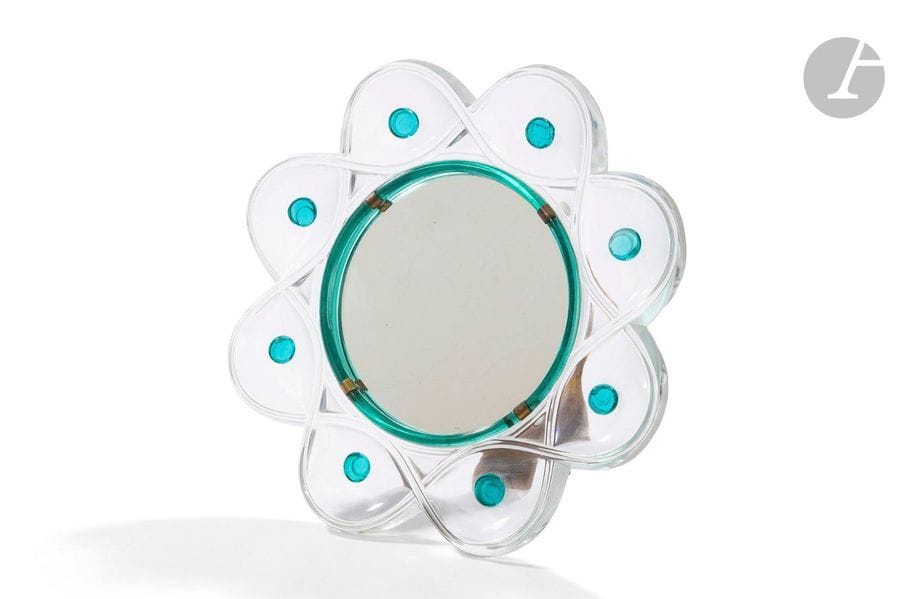 MARC LALIQUE (1900-1977) POUR MAISON LALIQUE
Miroir à poser. Épreuve en cristal clair; les cabochons et le cercle intérieur en cristal teinté émeraude. Chevalet en laiton. Petites égrenures en pourtour. Signé LALIQUE France en gravure sur le pourtour. D. 27,8cm