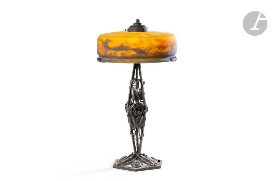MULLER FRÈRES LUNÉVILLE & TRAVAIL FRANÇAIS
Lampe de salon. Le pied en fer forgé et patiné. L’abat-jour circulaire en verre marmoréen polychrome rapporté et non d’origine. Cache central sur l’abat-jour en fer forgé. Un accident sur la gorge de l’abat-jour. La verrerie signée MULLER Fres Lunéville. H.48cm – D. 26cm