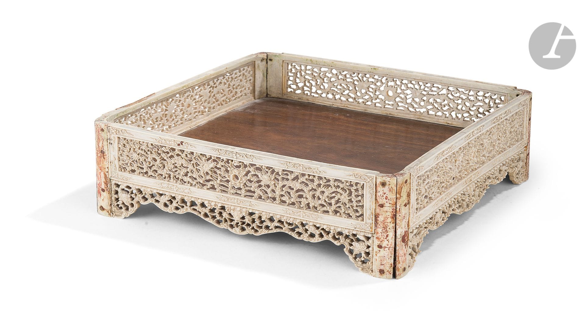 Wood and ivory square tray, Vietnam or China for Vietnam, 19th centuryThe
sides lined with rectangular plates of finely openwork ivory decorated with dragons in the clouds in pursuit of the sacred pearl. The pearl is symbolized in the center of the decoration by a missing mother-of-pearl element. The frame of the openwork part is solid and decorated with flowers and foliage. At the base of each plate is another openwork element decorated with dragons in the clouds and a turtle at each end. The four assembled plates form a vertical foot at each corner, which was originally reinforced with silver or gold spandrels (as suggested by a small element that has remained glued), which have now disappeared. Old collection label with a scratched inscription glued underneath.
Height: 7.2 cm; 25 x 25.5 cm; gross weight: 593 g

