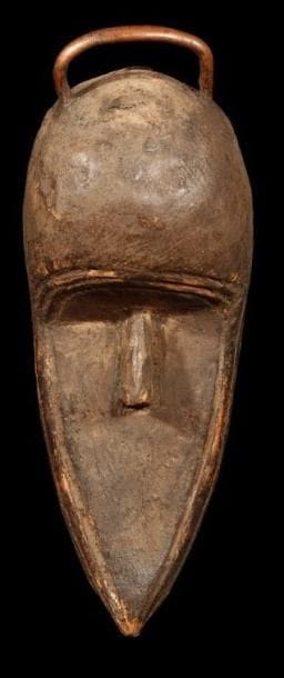 Masque TOMA (Guinée) "Masque" sans yeux et sans bouche, au menton très allongé, pointu, scarifications entourant le visage. Poignée de cuivre sur le haut du crâne. L'intérieur du masque est rempli de matières sacrificielles ce qui laisse à penser que ce masque non porté servait de reliquaire. Hauteur: 32 cm.