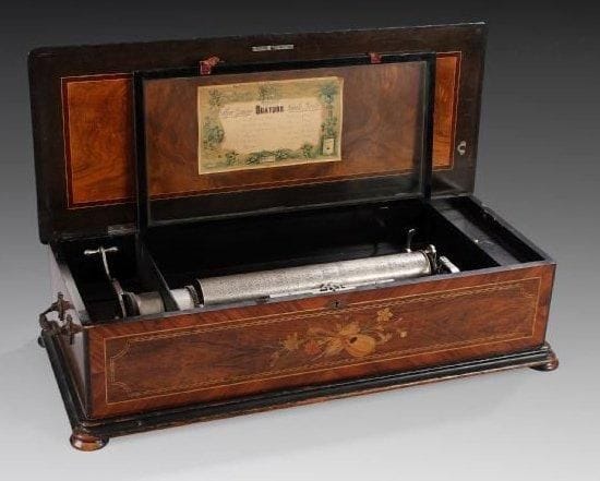 «Boîte à music». Cylindre à picots en métal simple à six airs. Fabriqué par Ch. Ullmann (Paris - St Croix en Suisse). Vers 1890. Un peigne métal sans manque. Le mouvement est contenu dans une boîte en bois à belle marqueterie de fleurs. Deux larges poignets en bronze permettent son transport. Hauteur: 25 cm - Largeur: 95 cm Profondeur: 25 cm Bel état, 90%.