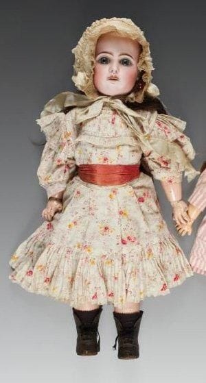 Bébé JUMEAU, tête en porcelaine. Marquée au tampon rouge «tête JUMEAU, T.10», (fêlure derrière l'oreille jusqu'au menton), yeux fixes bleus, bouche ouverte sur une rangée de dents, oreilles percées, perruque brune. Corps articulé en bois et composition marqué au tampon bleu «bébé Jumeau, diplôme d'honneur», (manque un petit doigt d'une main). Robe en coton beige à fleurettes, bonnet et bottines. Hauteur: 58 cm