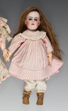 Bébé JUMEAU, tête porcelaine. Marquée au tampon rouge «tête JUMEAU T.7», (fêlure derrière la tête), yeux fixes bleus, bouche ouverte sur une rangée de dents, oreilles percées, perruque châtain clair. Corps articulé en bois et composition portant l'étiquette bleue «bébé JUMEAU diplôme d'honneur». Robe en coton rayé rose et blanc, bottines. Hauteur: 45 cm