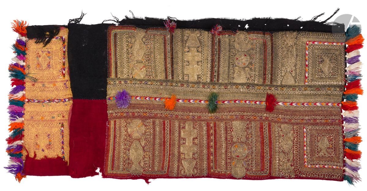 Fragment de tunique de mariée, kiwa al-kabira, Tunisie, XIXe - XXe siècle
Deux lés de laine rouge et noire tissés puis cousus ensemble et brodés de fils métalliques garnis de perles et de sequins formant différents registres rectangulaires garnis de motifs floraux stylisés ou de poissons. Décor rehaussé de fils de soie multicolores brodés et noués en floches formant deux lignes l’une bordant un côté, l’autre disposée au quart supérieur. 
On joint une paire de chaussures, Empire ottoman, XIXe siècle, en cuir recouvert de velours vert brodé de fils métalliques ponctués de sequins. Longueur : 24,7 cm ; usures.
110 x 51 cm
Quelques trous. 

Ce genre de pièce au fin travail de broderie et couleurs chatoyantes venait agrémenter l’avant des tuniques de mariée tunisiennes en guise de plastron.

A section of a bridal dress, kiwa al-kabira, Tunisia, 19th-20th century

