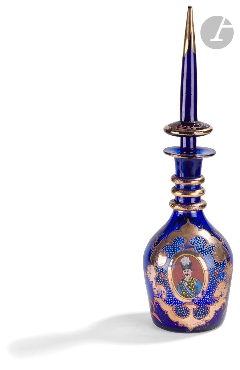 Grande carafe couverte à l’effigie de Nâser al-Dîn Shâh Qâjâr (r. 1848-1896), Bohême pour l’Orient, XXe siècle
En verre transparent de teinte bleu cobalt à décor peint en polychromie et doré de deux médaillons chantournés, l’un renfermant un portrait du sultan qâjâr Nâser al-Dîn Shâh en costume de cérémonie avec ses décorations et sa coiffe à aigrette, l’autre une tige florale.
Hauteur totale : 49,5 cm 
Décor et dorure partiellement effacés, éclat à la base du bouchon.

A Bohemian glass bottle and tapering stopper decorated with a portrait medallion of Nasir al-Din Shah Qajar (r. 1848-1896), Iran, 20th century

