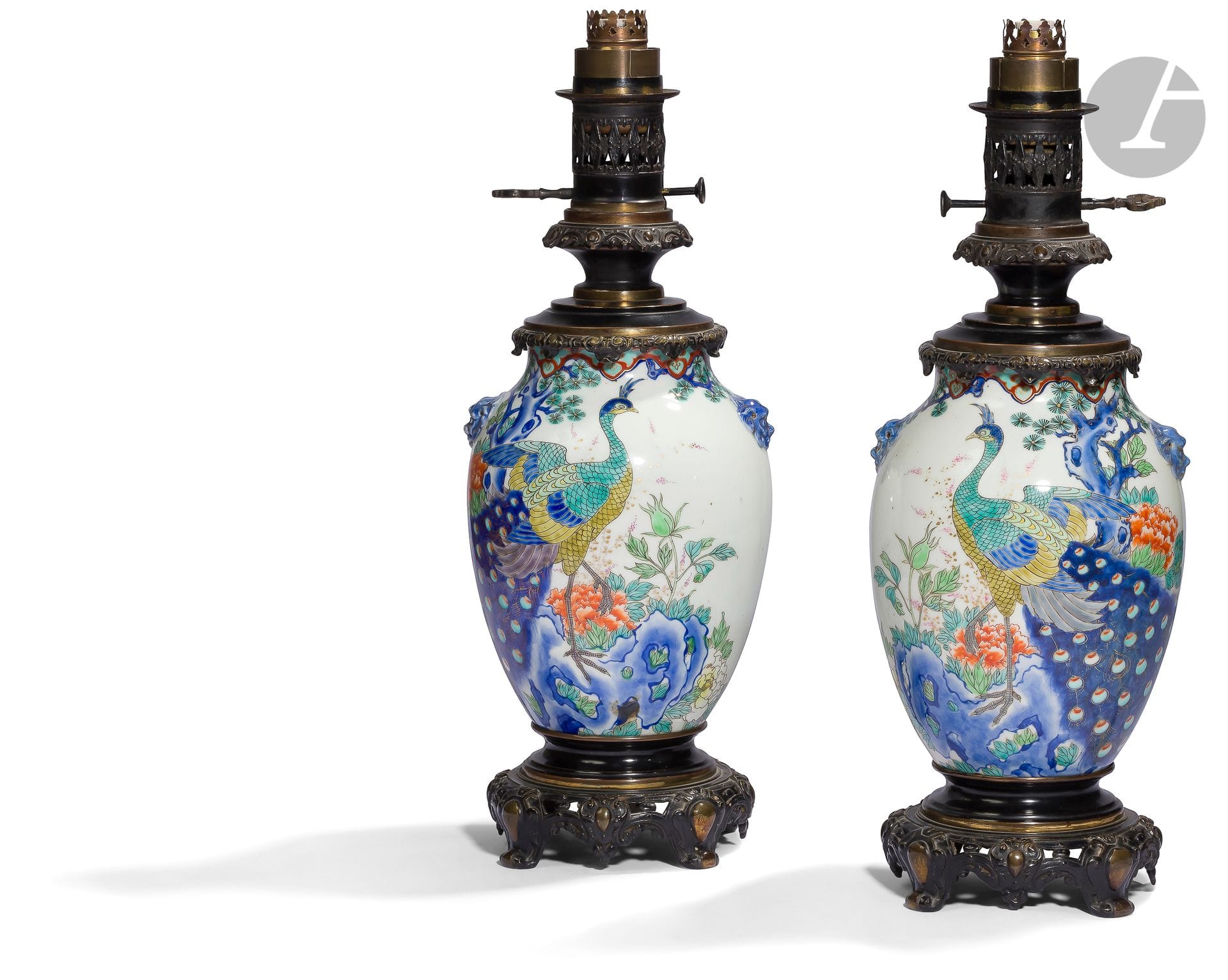 Japon
Paire de vases en porcelaine d’Arita, fours secondaires d’Imari, probablement Fukagawa ou Koransha. Ils sont de forme ovoïde en porcelaine blanche émaillée polychrome à décor d’un couple de paons sous un pin et entouré de fleurs diverses, pivoines, chrysanthèmes, etc.. Les côtés des vases sont ornés de deux mascarons en forme de tête de shishi, émaillés en bleu sous couverte rehaussés d’un léger émail doré.
Les vases ont, en Europe, été transformés en lampe à pétrole à l’aide d’une monture en bronze fixée au pied et au col. Ils ont par la suite été montés à l’électricité.
Époque Meiji (1868-1912).
Fond des vases percé.
H. totale : 52,5 cm