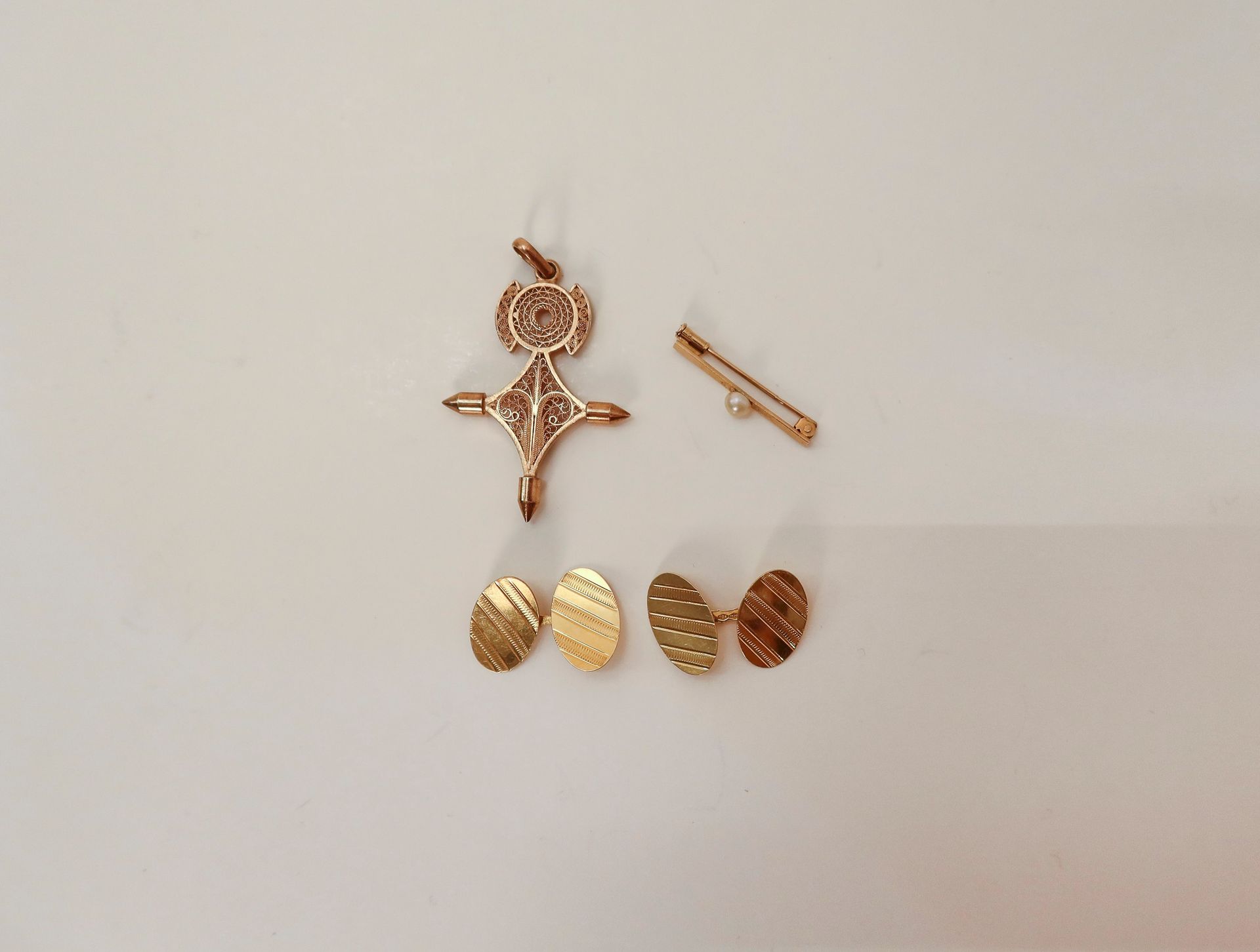 
Lot de bijoux en or (diverses teneurs). Poids : 15,4 g

- 1 petite épingle à nourrice en or (18K) sertie d'une perle

- 1 paire de boutons de manchettes en or (18K)

- 1 pendentif croix saharienne filigranée en or (14K). Poids : 9,2 g 
