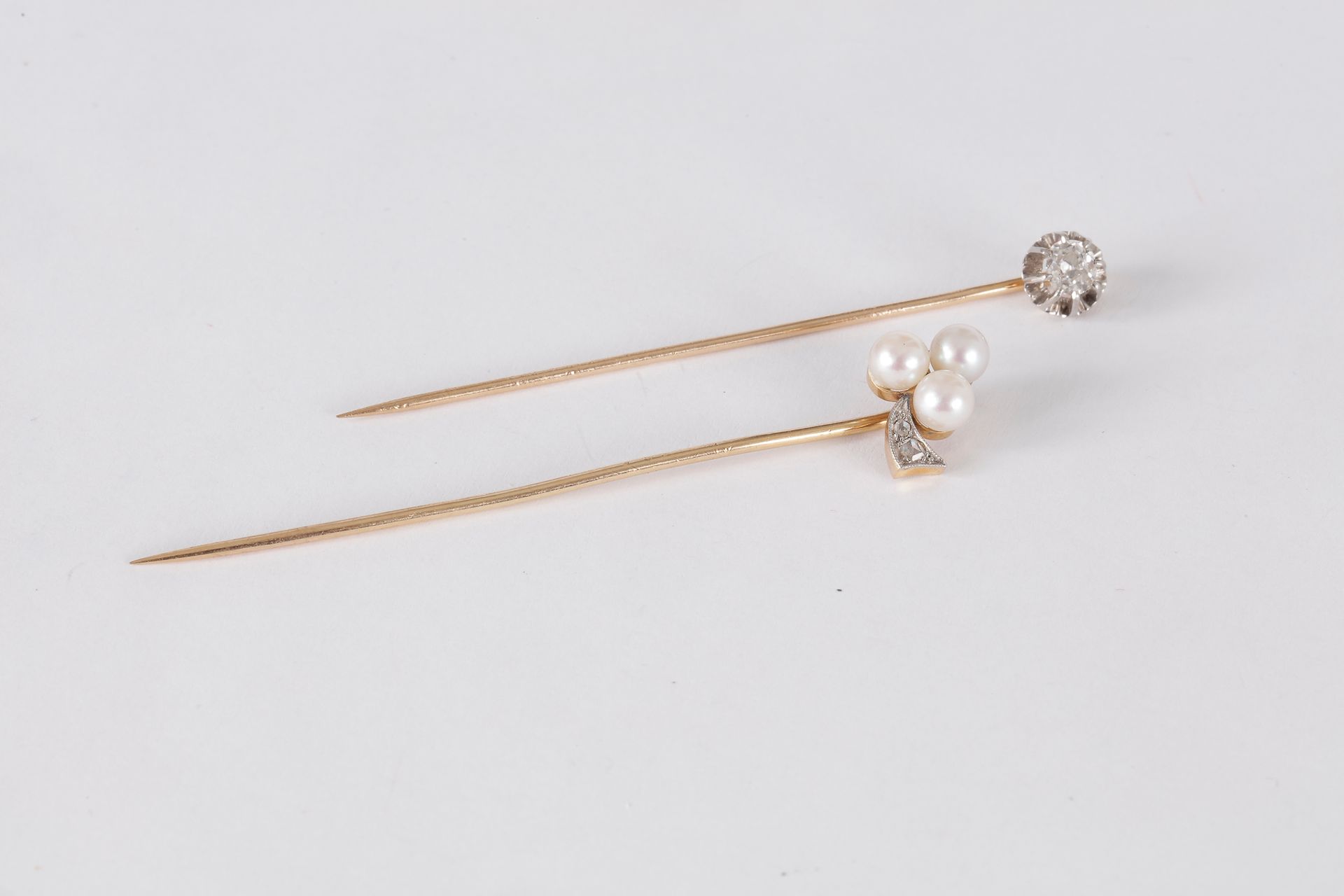 Lot de deux épingles de revers en or 18K (750), l’une sertie d’un diamant de taille ancienne, l’autre ornée de 3 perles et de diamants taillés en roses.

Poids brut : 4,1 g (égrisures)