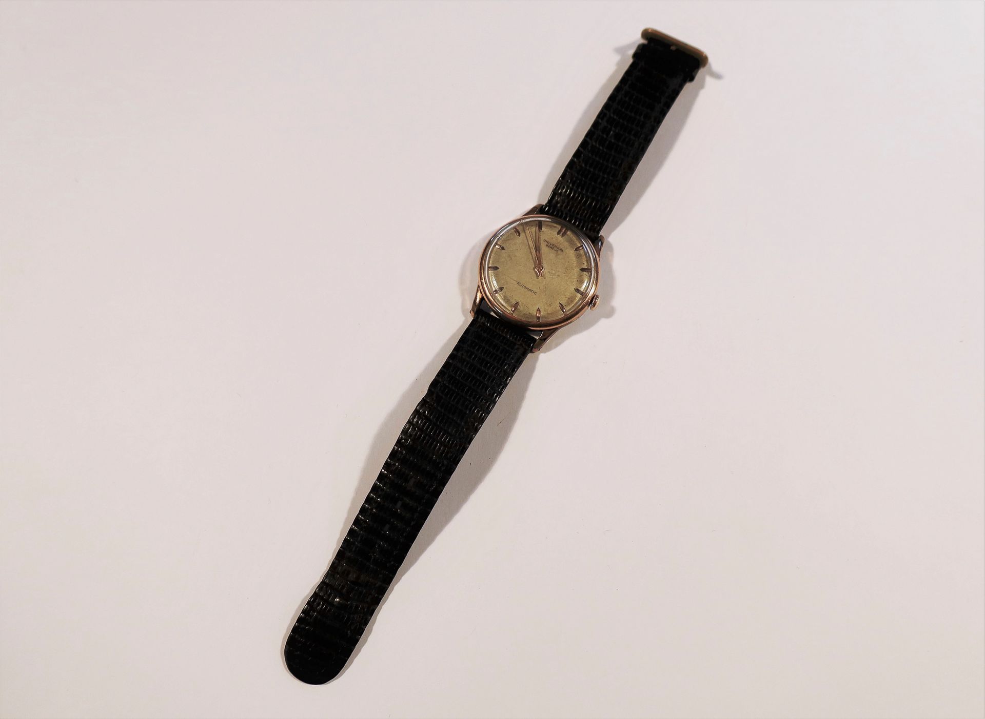 UNIVERSAL 

N°1290364

Montre bracelet pour homme en métal doré, cadran blanc (piqué), index bâtons appliqués formant les heures, mouvement à remontage mécanique.