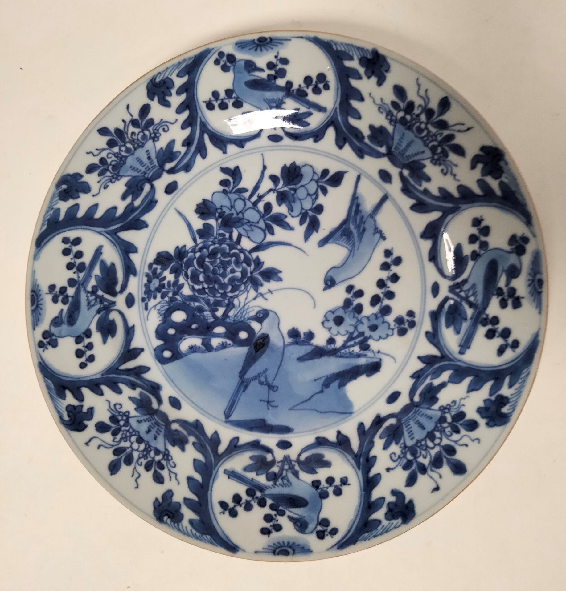 CHINE, époque KANGXI (1662 - 1722)
Assiette ronde en porcelaine émaillée en bleu sous couverte dans un médaillon central et en réserve de pies parmi les rochers fleuris, perchées et en vol, et des bouquets fleuris. 
Diamètre : 22,2 cm