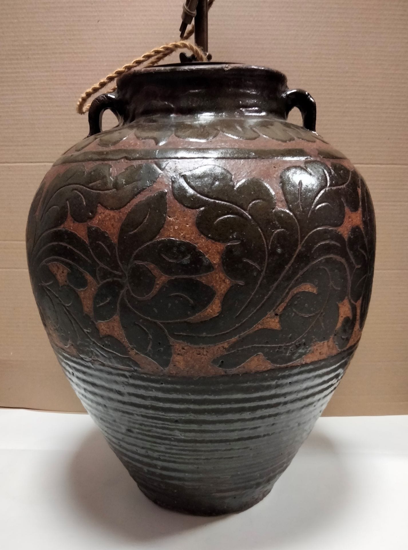 CHINE, XXe siècle, dans le goût des fours de Cizhou
Jarre à deux anses en grès émaillé brun, la panse à décor dégagé en léger relief de fleurs, poissons et rinceaux feuillagés sur fond marron, surmontée d'une frise de palmettes. 
Hauteur : 50 cm
Montée en lampe, restaurations.