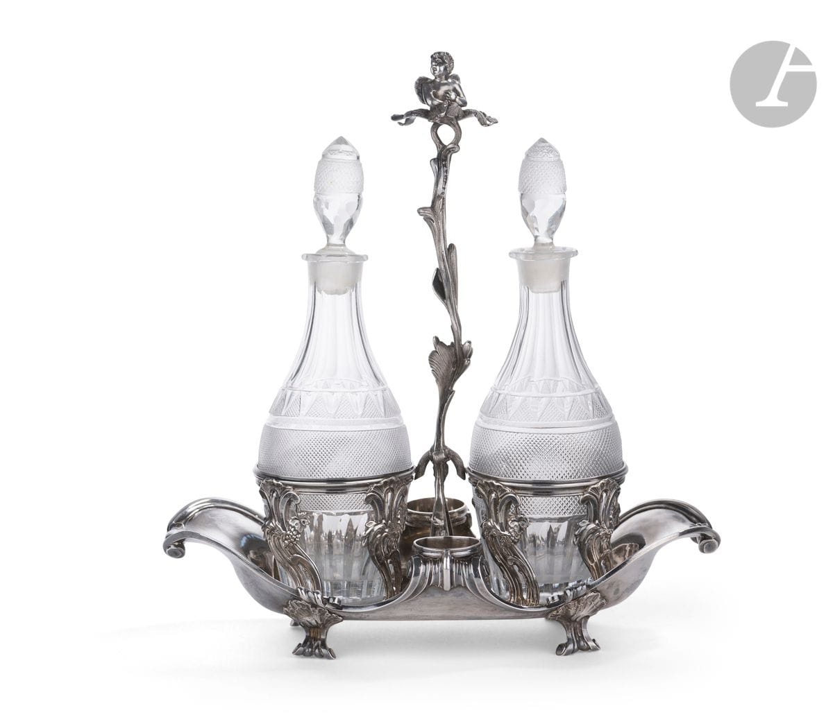 PARIS 1762 - 1768
Huilier vinaigrier en argent fondu et estampé de forme gondole. Il repose sur quatre pieds à enroulements à agrafes de coquille. Les porte-carafes sont estampés de motifs de raisins et de feuillages. La tige centrale, postérieure, figure un feuillage torsadé sommé d’un putto en ronde bosse sur une terrasse de feuilles. Le corps est gravé de lettres gothiques : AD
Maître orfèvre : Jean-Baptiste-François CHERET, reçu en 1759
Poinçon : pas de maison commune visible 
État : modification postérieure de la partie centrale et paire de carafes du XIXe siècle en verre du Creusot
Poids : 916 g - longueur : 27,5 cm - hauteur : 29,9 cm
