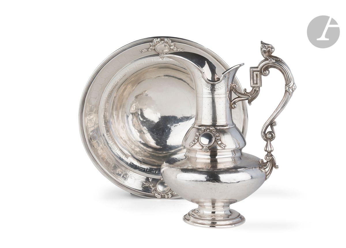 PARIS ÉPOQUE NAPOLÉON III
Aiguière de toilette et son bassin en argent de forme circulaire ciselés sur plusieurs registres de rangs de points, de fleurs et de frises de grecques sur des fonds amatis, rehaussés d’appliques de nœuds de rubans encadrant des médaillons libres de gravure rapportés. Anse en console, feuillages, rangs de filets et tête de lion en ronde-bosse.
Orfèvre : Auguste-Louis FIZAINE, insculpe en 1859
Poinçon tête de mercure pour l’exportation
Poids : 2712,8 g - hauteur : 38,5 cm - diamètre : 40 cm