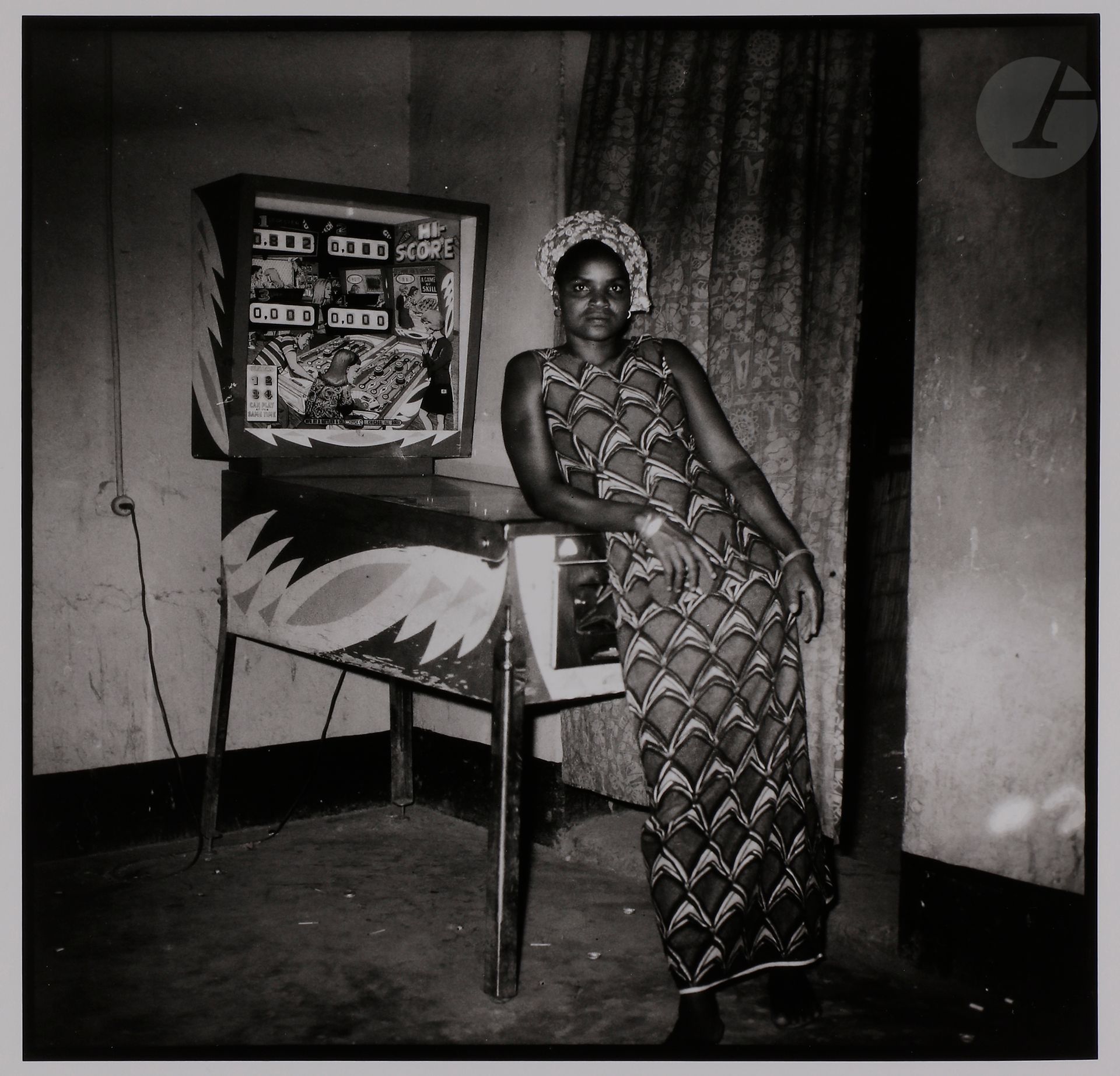 Philippe Koudjina (1940-2014) 
Niamey. Niger, c. 1960-1970. 
Jeune fille accoudée au flipper. 
Épreuve argentique (2002), signée à l’encre dans la marge inférieure à droite. Tampon et signature du tireur Philippe Salaün, date du tirage au verso. 
Image : 26,5 x 26,5 cm 
Feuille : 40,5 x 30,5 cm

Philippe Koudjina (1940-2014) 
Niamey. Niger, c. 1960-1970. 
Young girl leaning on pinball machine. 
Gelatin silver print (2002), signed in ink in the lower right margin. Stamp and signature of the printer Philippe Salaün, date of print on verso. 
Image: 26,5 x 26,5 cm 
Paper : 40,5 x 30,5 cm