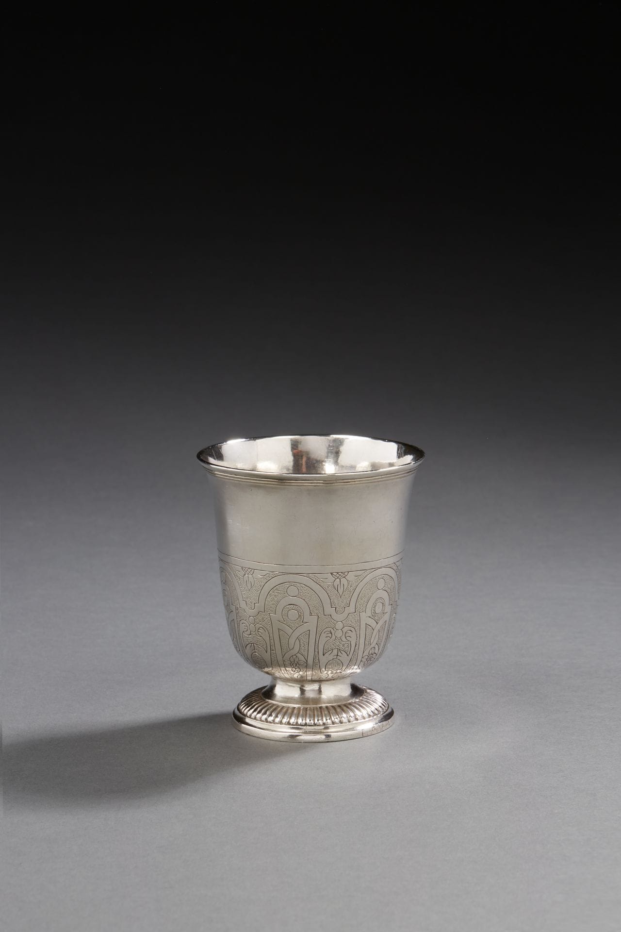 MORLAIX 1722 - 1727
Timbale tulipe en argent sur piédouche repoussé de godrons gravé LAVAL en bordure, le corps gravé jusqu’en partie médiane de lambrequins de tailles alternées dans des arcatures sur fond amati, la bordure moulurée de filets.
Maître orfèvre : Mathurin HELIES, reçu en 1731
Poids : 98,2 g - hauteur : 8,6 cm 
État : rayures d’usage
MORLAIX 1722 - 1727
A silver tulip tumbler
Master silversmith: Mathurin HELIES
