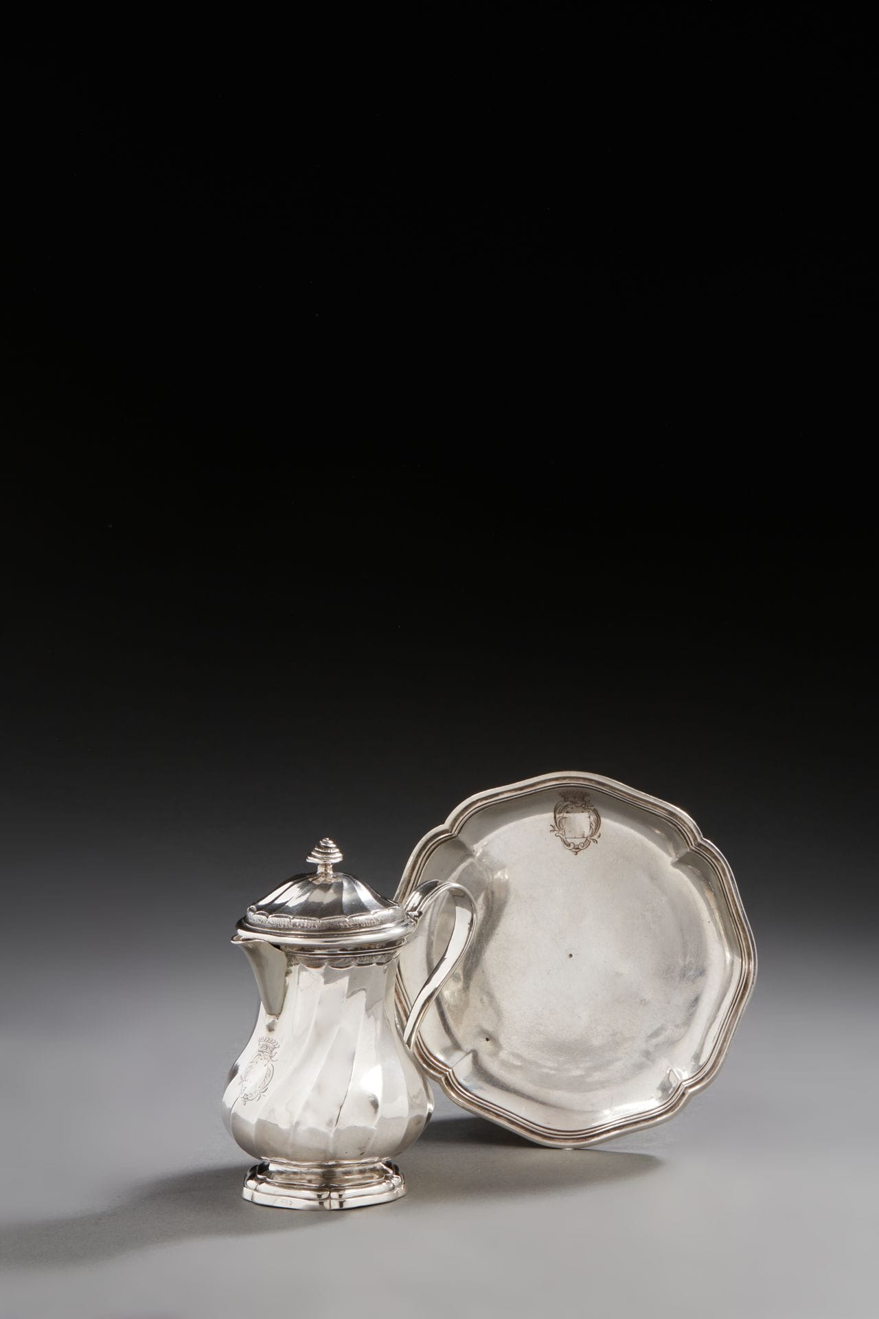 TOULOUSE 1763 et 1762 - 1768
Moutardier / crémier en argent et son présentoir. Modèle à côtes torses posant sur un piédouche à contours en dégradés. Les côtes sont délimitées par un fond amati dit « décor chauve-souris », en rappel sur le haut du corps et le couvercle à charnière, sommé d’un colimaçon. L’anse à deux points d’accroche est bordée de filets. Le plateau, à quatre contours, mouluré de filets, pose sur une bâte. Le plateau et le moutardier sont gravés d’armoiries comtales dont le champ a été dégravé.
Maître orfèvre : Jean GAILHARD, reçu en 1747
Poids : 305,9 g - hauteur : 11,5 cm - diamètre du présentoir : 12,6 cm
Poinçons : décharge uniquement sur le présentoir pour Toulouse 1762 - 1768, maison commune H pour le moutardier pour Toulouse 1763
TOULOUSE 1763 and 1762-1768
A silver mustard or cream pot and its platter
Master silversmith: Jean GAILHARD