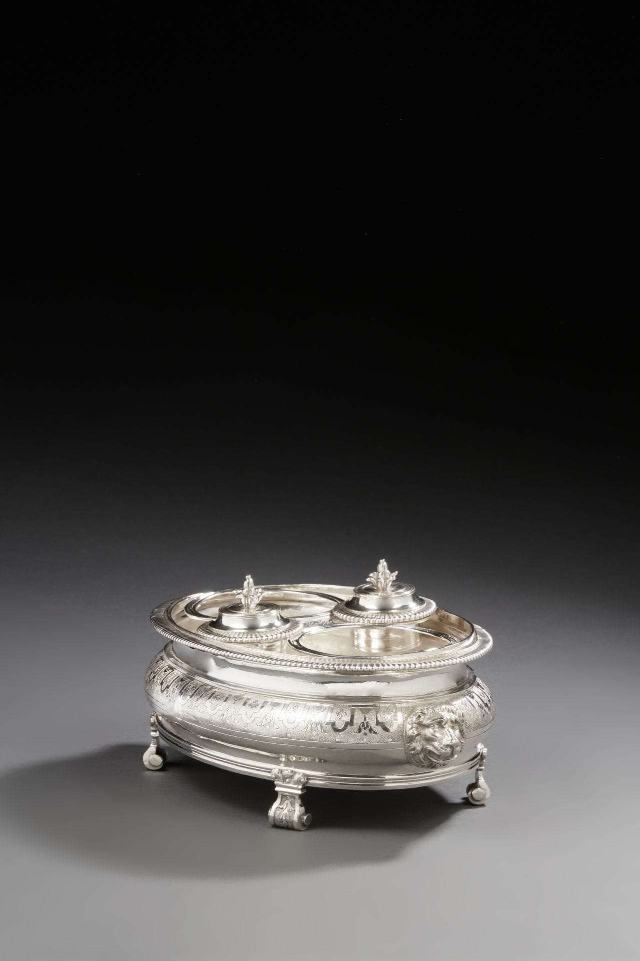 RENNES 1706 - 1707
Huilier vinaigrier en argent de forme ovale, il repose sur quatre pieds à enroulements ciselés de lambrequins sur fond amati en rappel sur le corps alternant chutes de fleurons et quartefeuilles, dont les prises figurent des têtes de lion au naturel. La bordure est moulurée de godrons, la grille mobile recevant les bouchons (non poinçonnés) est ciselée des mêmes motifs que le corps.
État : anciennes restaurations sur le corps
Maître orfèvre : Jean-Baptiste GERARD, reçu en 1679, décédé en 1712
Poids : 1084,2 g - longueur : 24,5 cm - hauteur : 11,7 cm
RENNES 1706 - 1707
An oval silver oil and vinegar cruet
Master silversmith: Jean-Baptiste GERARD