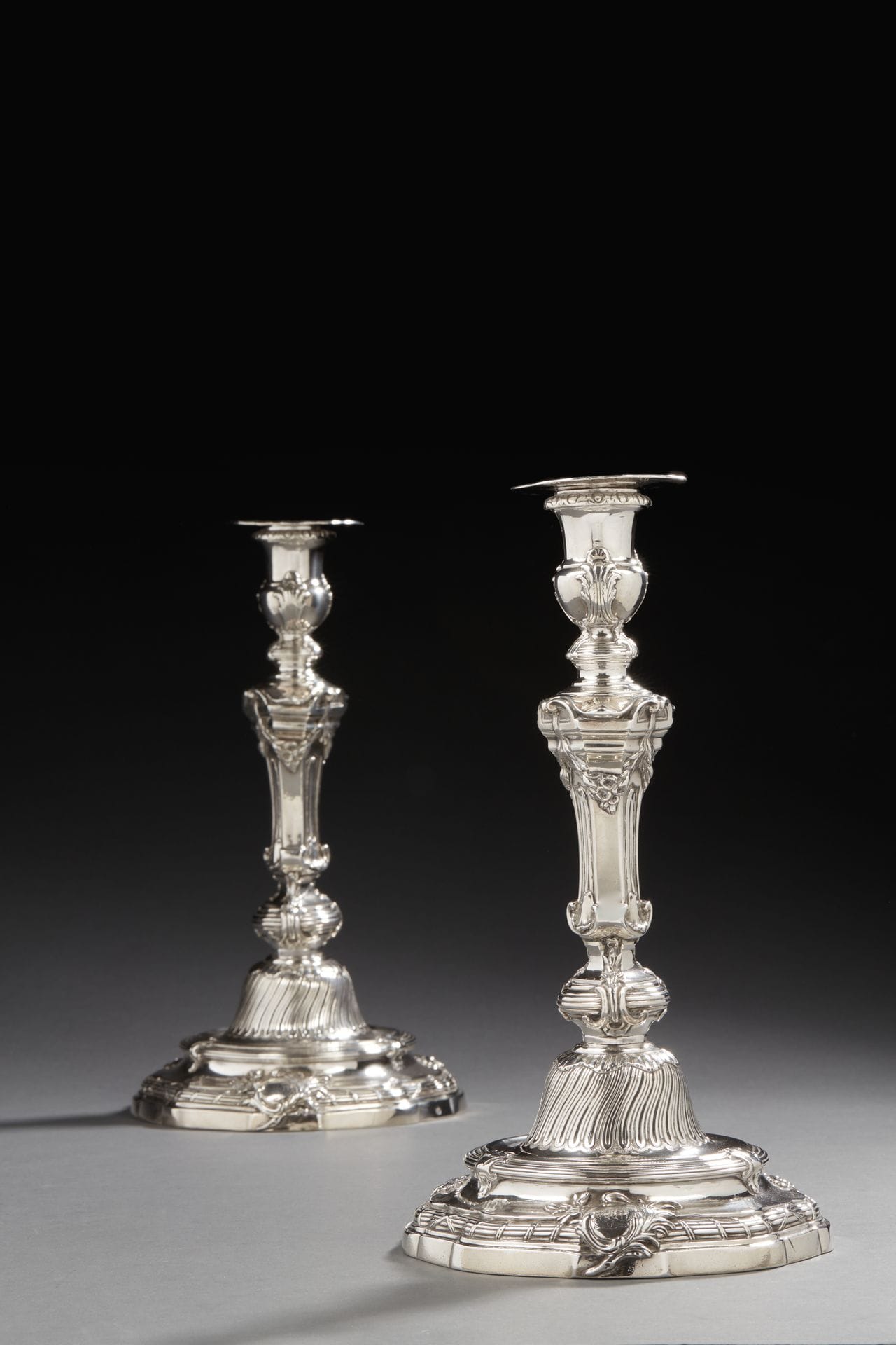 PARIS 1750 - 1751
A pair of silver torches and their wicks. They stand on a poly-lobed base with a double doucine moulded with nets and crossed ribbons on the first one, enhanced with three clasps on the second one as a reminder of the knot and the binet. It is engraved with a coat of arms surmounted by a marquis crown, in a medallion framed by palms and foliage. The umbilicus is decorated with twisted flutes. The hexagonal shaft alternates plain sides and lanceolate leaves topped by a garland rising from a capital. The tap, in the shape of a vase, is bordered by ovals.
On the reverse, the candleholders are engraved with the numbers N°2 and N°3 as well as the bobèches N°2 and N°4, indicating a probable series of six or twelve. 
 Master goldsmith : Alexis LOIR, received in 1733
Weight : 1907,1 g - height : 27,1 cm - diameter : 15,2 cm
Marks : the bobèches punched inside the master goldsmith, the charge, the common house and discharged on the cup, as well as the inside of the binet and on the reverse side
Condition : tears inside the bobèches
PARIS 1750 - 1751
A pair of silver candlesticks and their bobeches
Master silversmith: Alexis LOIR