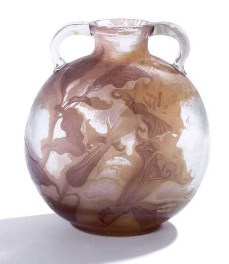 EMILE GALLE (1846-1904)
Important vase gourde à panse aplatie et à deux anses appliquées et modelées à chaud Etude en verre soufflé multicouche dégagé à l'acide à décor, parme, beige et mauve dégradé, de brugmansias, sur fond translucide légèrement marbré. Fêle démarrant au col et se poursuivant jusqu'à la moitié de la panse Vers 1900 Signature gravée en camée à l'acide et mention Etude gravée Hauteur: 29 cm